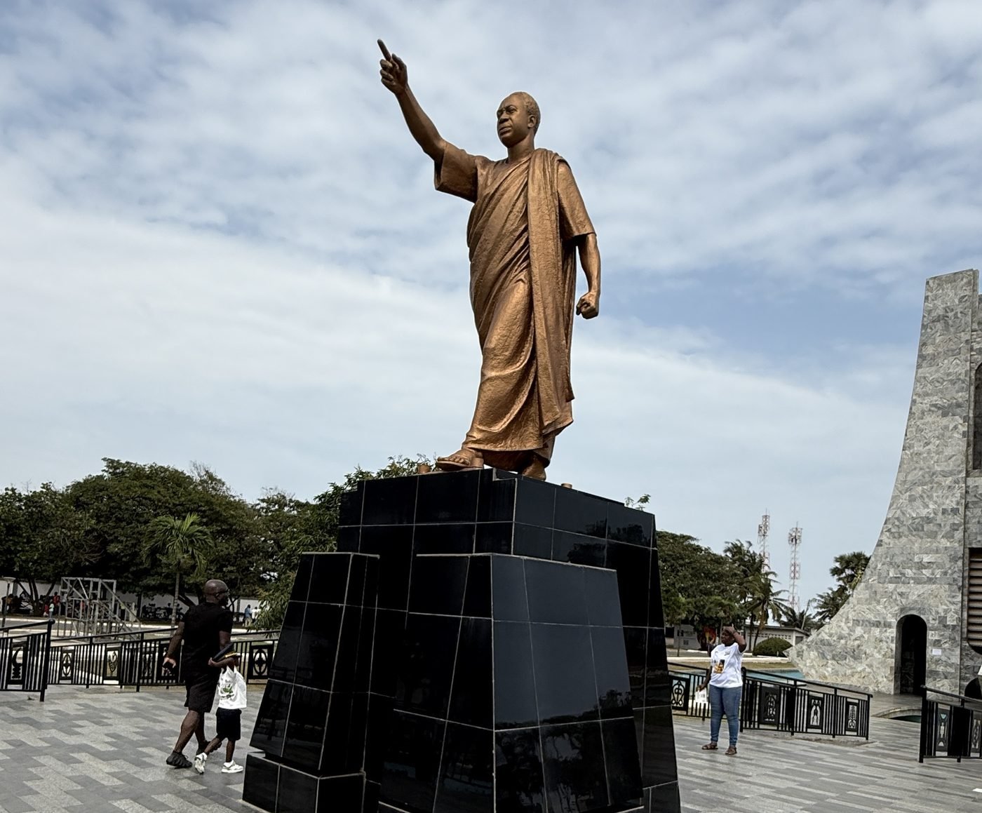 The bronze statue of Kwame Nkrumah pointing skyward at the Kwame Nkrumah Memorial Park in Accra, as visitors walk past its base